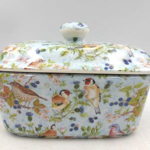 May include: A ceramic bread bin with a lid, decorated with a light blue pattern of birds, flowers, and berries. The lid has a small, round handle. The design is detailed and colourful, suitable for kitchen storage.