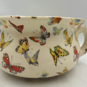 May include: A trio of speckled cream ceramic mugs, each adorned with a hand-painted floral design in blue, green, and yellow hues. The mugs have a simple, rounded form and a comfortable handle. Ideal for tea or coffee.
