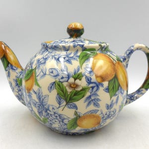 以下が含まれることがあります： レモン柄の青い花柄が施された白い陶器製のティーポット。ティーポットは丸いボディと湾曲した注ぎ口を持っています。