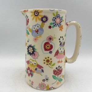 May include: A white ceramic jug with a floral and owl design. The jug has a handle and a wide mouth.
