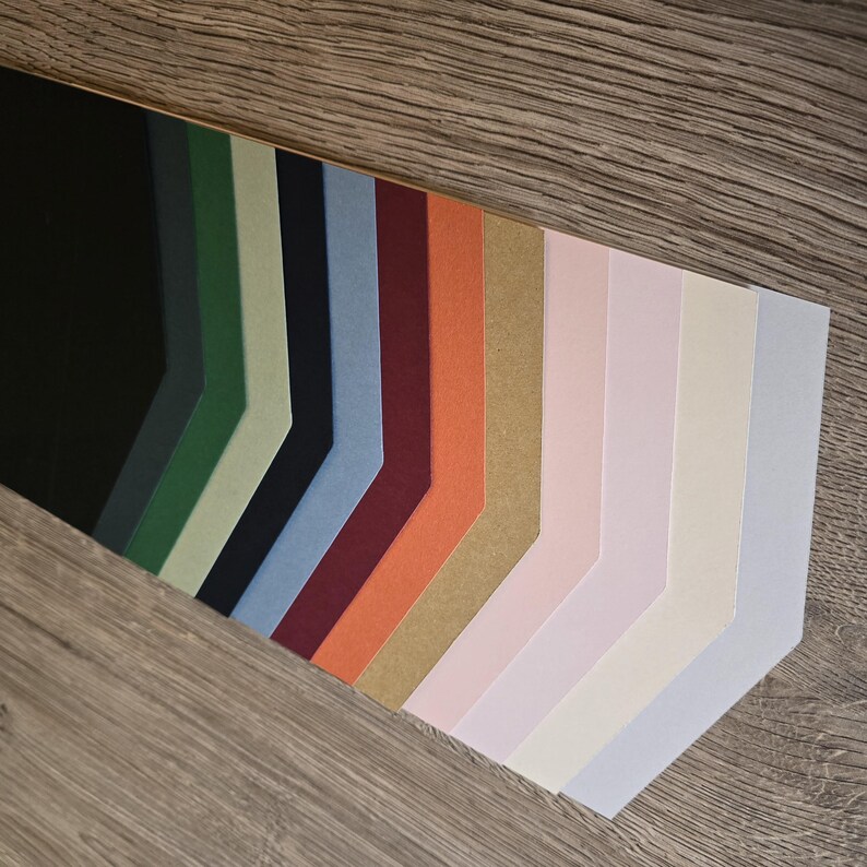 May include: A variety of cardstock paper samples in different colors, including black, green, blue, red, orange, brown, pink, white, and light blue. The paper is arranged in a fan shape, with the darkest colors at the top and the lightest colors at the bottom.