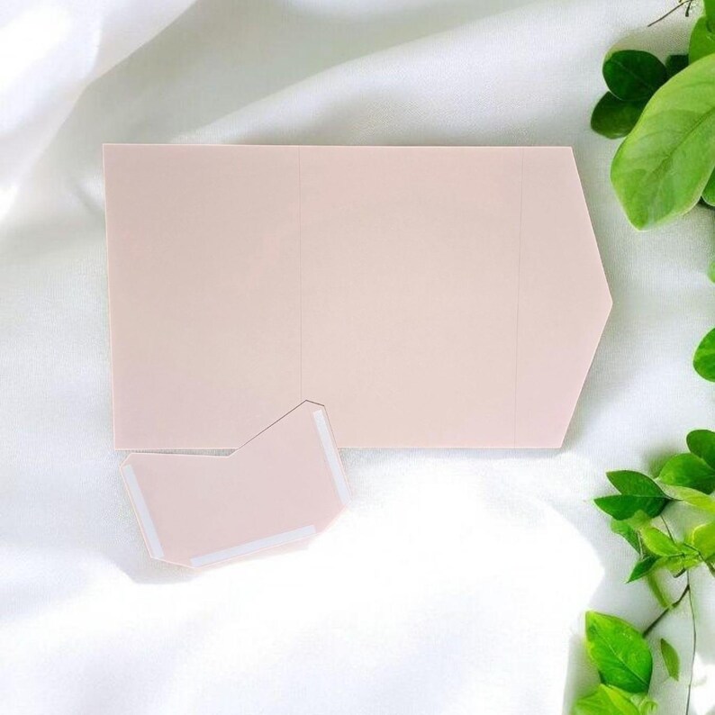 May include: A pale pink, folded card with a slightly pointed edge. The card is blank and has a small, folded flap on the bottom.