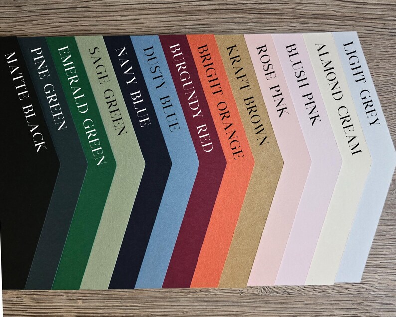 May include: A selection of paper samples in various colors, including light grey, almond cream, blush pink, rose pink, kraft brown, bright orange, burgundy red, dusty blue, navy blue, sage green, emerald green, pine green, and matte black.