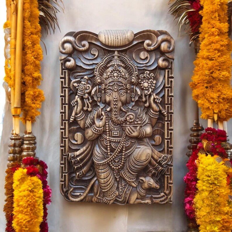 May include: A carved wooden plaque depicting the Hindu deity Ganesha. The plaque is brown and features intricate details, including Ganesha's elephant head, trunk, and four arms. The plaque is surrounded by a decorative border.