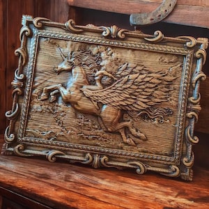 May include: A wooden carving of a winged unicorn in a decorative frame. The unicorn is depicted in a running pose with its wings spread out. The carving is detailed and realistic, with visible wood grain.