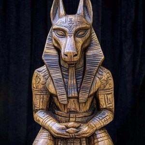 K&ouml;nnte beinhalten: Eine Holzstatue von Anubis, dem &auml;gyptischen Gott der Toten, mit einem Schakal-Kopf und einem menschlichen K&ouml;rper. Die Statue ist mit komplizierten Details geschnitzt und hat eine dunkelbraune Oberfl&auml;che.