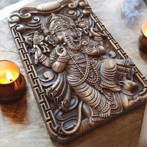 May include: Intricately carved wooden wall hanging featuring the Hindu deity Ganesha. The sculpture depicts Ganesha with his elephant head, multiple arms, and a rat at his feet. The wood is dark brown and has a rich, polished finish.