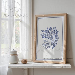 May include: A framed print with a blue coral design and the text "The Beach Club" on a white background. The frame is light wood. The print is displayed on a white shelf with a white ceramic pitcher and a decorative ball.