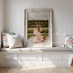 Può includere: Una grande stampa incorniciata con finitura bianca anticata, raffigurante una persona con un vestito rosa seduta su una coperta. Due cuscini floreali e un cuscino neutro poggiano su una seduta finestra. La scena è ambientata in una stanza luminosa e ariosa.