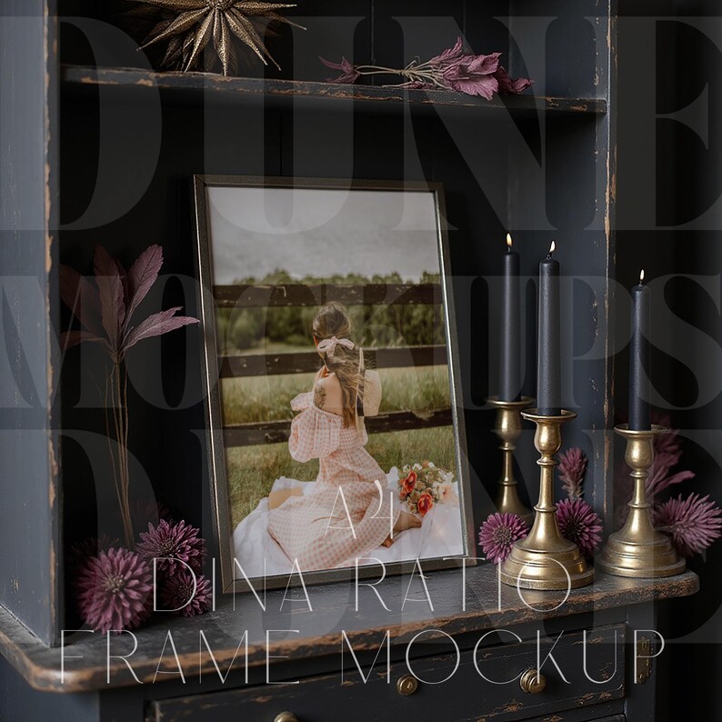 Pu&ograve; includere: Un mockup fotografico incorniciato con una cornice nera, con una persona in un vestito rosa. La cornice poggia su un mobile grigio scuro, adornato con candele, candelabri in ottone e fiori decorativi viola. Il testo "DINA RATIO FRAME MOCKUP" &egrave; visibile.