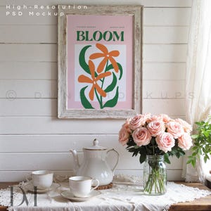 May include: A framed poster with the word "BLOOM" and orange flower illustrations hangs above a table set for tea. A bouquet of pink roses sits in a glass jar, and a white teapot and teacups are on the table.