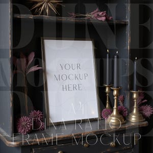 Pu&ograve; includere: Mockup di cornice A4 dorata con il testo "YOUR MOCKUP HERE" su una superficie di legno scuro. Candele nere in candelabri dorati e fiori decorativi completano la scena.