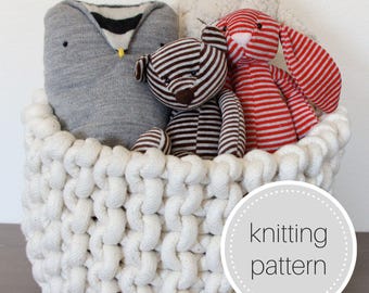May include: A white crocheted basket filled with stuffed toys, including a gray owl, a brown and white striped teddy bear, and a red and white striped bunny. The basket has a label that says "knitting pattern".
