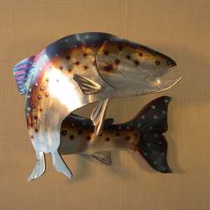 May include: Two metal trout fish sculptures, one jumping over the other. The fish are silver with brown spots and blue accents. The larger fish has the text "Jay Z.  Poulin" on its side.