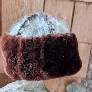 May include: A brown fur hat featuring a dark brown fur band and a top section of white and grey fur. This hat is a winter accessory, designed for warmth and style.