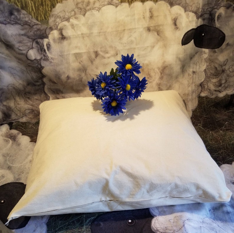 May include: A white cotton pillow with a zipper closure. The pillow is on a patterned fabric background with a bouquet of blue flowers with yellow centers.