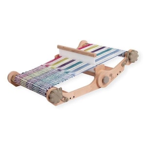 May include: A wooden loom with a colourful woven fabric on it. The loom has two wooden spools and a wooden frame. The fabric is woven with a variety of colours, including blue, green, purple, and pink.