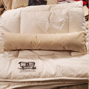 May include: A white down comforter with a white wool filled bolster pillow and a white wool filled pillow with a black and white sheep illustration and the text "theshepherdspillow.com 100% Wool Filled Pillow & Duvets".