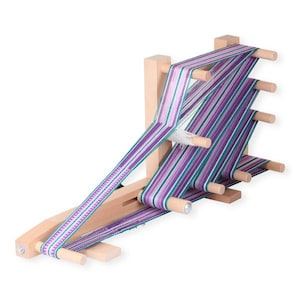 May include: A wooden loom with purple and green yarn woven on it. The loom has a wooden frame and multiple pegs for holding the yarn.