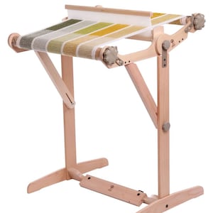 Peut inclure: Un métier à tisser en bois avec un tissu tissé coloré tendu sur le dessus. Le tissu présente des rayures vertes, jaunes et blanches. Le métier à tisser a des pieds en bois réglables et des boutons pour le contrôle de la tension. Pour les projets d'art textile.