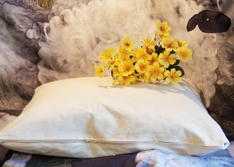 May include: A white pillow with a zipper closure, sitting on a patterned fabric background. A bouquet of yellow flowers is resting on top of the pillow.