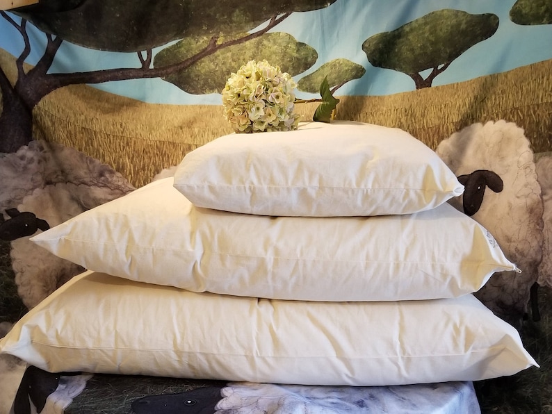 May include: Three white cotton pillows stacked on top of each other. The pillows are all the same size and shape, and they are all made of a soft, natural material.