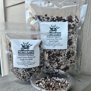 May include: Three clear plastic bags and a small clear container filled with carnivorous plant soil. The bags have white labels with the text "BOTANY PLANTS" and "TANY PLANTS". The soil is a mix of dark and light-colored materials.