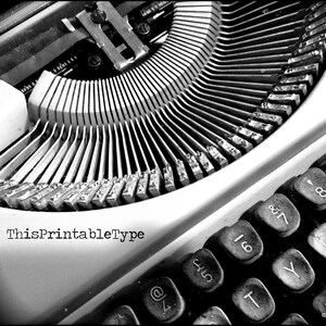 May include: Black and white close-up image of a vintage typewriter with the text "ThisPrintableType" on the front. The keys are visible and include numbers, symbols, and letters.