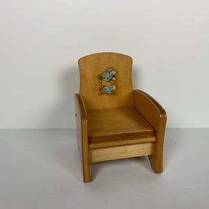 May include: A small wooden chair with a light brown finish. The chair has a curved back and armrests. A colorful decal of a cartoon bunny holding a carrot is on the backrest. The chair is designed for a child.