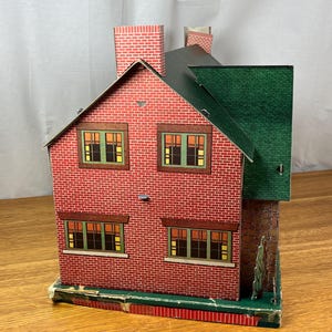 May include: A vintage-style toy dollhouse constructed from printed cardboard, featuring a red brick exterior pattern, a dark green roof, and a prominent chimney. The structure includes four rectangular windows with green frames and yellow interior panes.