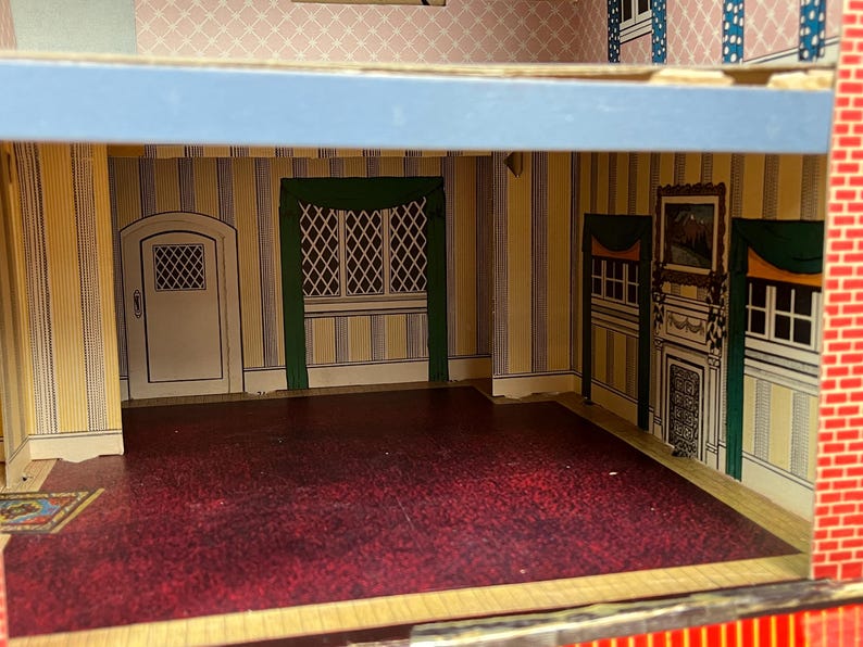 May include: A dollhouse interior featuring a room with yellow and blue striped wallpaper, a dark red floor, and a white door. The walls include printed details of a fireplace, green curtains, and a window with a lattice pattern design.