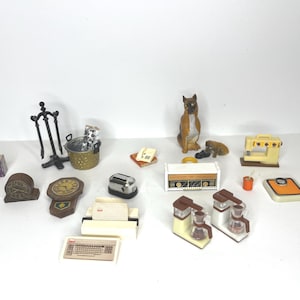 Peut inclure: Une collection d'objets miniatures pour la maison, dont un grille-pain, une cafetière, une radio, une horloge et une figurine de chien. Les objets sont disposés sur une surface blanche.