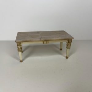 Puede incluir: Una mesa blanca con una tapa de mármol marrón claro y detalles dorados. La mesa tiene cuatro patas y una forma rectangular.