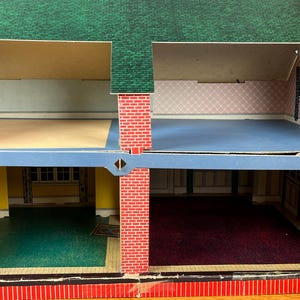 May include: A two-story dollhouse with a green shingled roof and red brick exterior walls. The interior features four rooms with printed wallpaper, including yellow, pink, and white patterns, and floor coverings in green, blue, and dark red.