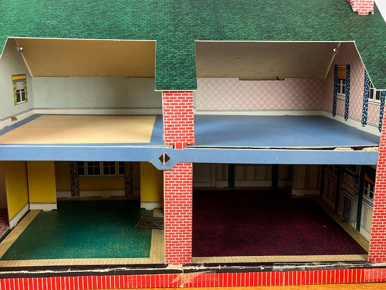 May include: A two-story dollhouse with a green shingled roof and red brick exterior walls. The interior features four rooms with printed wallpaper, including yellow, pink, and white patterns, and floor coverings in green, blue, and dark red.