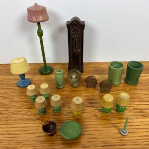 May include: A collection of miniature wooden dollhouse furniture including a tall floor lamp with a pink shade, a dark brown grandfather clock, a blue table lamp, several small lamps with yellow shades, green cups, and various small wooden accessories.