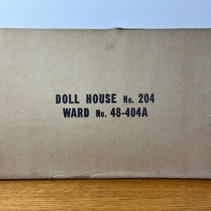 May include: A rectangular cardboard box with a tan finish. The center of the box features black printed text that reads DOLL HOUSE No. 204 and WARD No. 48-404A. The box appears to be a storage container for a toy set, showing signs of wear on the edges.