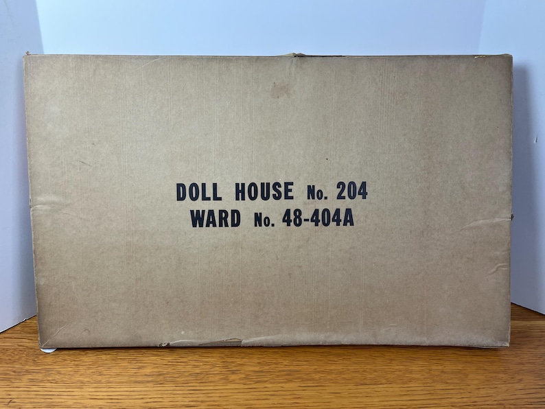 May include: A rectangular cardboard box with a tan finish. The center of the box features black printed text that reads DOLL HOUSE No. 204 and WARD No. 48-404A. The box appears to be a storage container for a toy set, showing signs of wear on the edges.