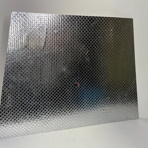 May include: A silver, diamond-patterned, heat-resistant sheet with a small hole in the center.