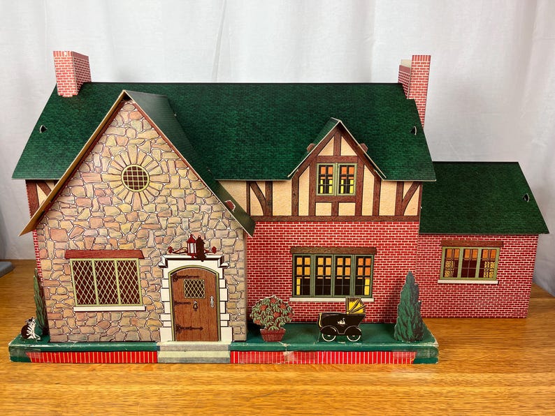 May include: A toy dollhouse featuring a green roof, a stone-patterned facade on the left section, and red brick-patterned walls on the right. The structure includes a brown front door, multiple windows with lattice details, and a small toy carriage.