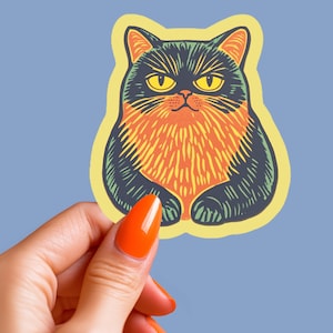 May include: A sticker of a black and orange cat with yellow eyes. The cat is sitting with its paws tucked in and has a grumpy expression.