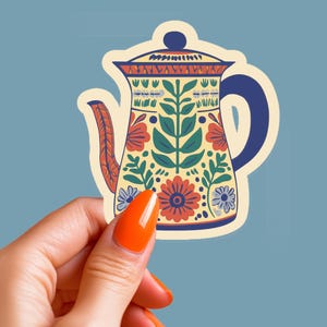 Peut inclure: Une théière en céramique à motif floral coloré avec une poignée bleue. La théière est jaune avec des motifs floraux rouges, bleus et verts.