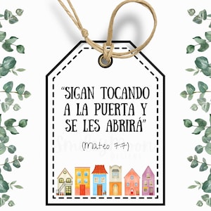 May include: A white gift tag with a black border and a quote in Spanish that reads "SIGAN TOCANDO A LA PUERTA Y SE LES ABRIRA" (Mateo 7:7). The tag is decorated with a row of colorful houses.