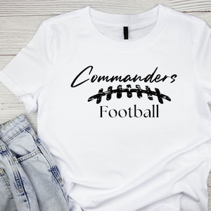 May include: White t-shirt with black text that reads "Commanders Football" and a stylized football graphic.