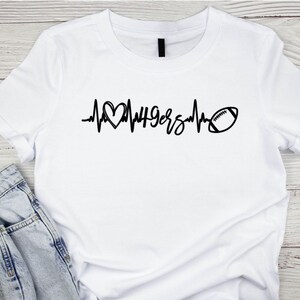 May include: White t-shirt with a black graphic design. The design features a heart, the word "49ers", a heartbeat line, and a football. The shirt is made of a soft material and is suitable for casual wear.