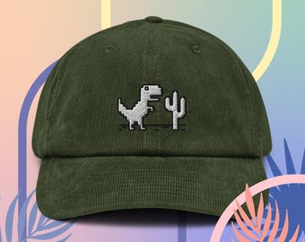 May include: A green corduroy baseball cap with an embroidered image of the classic 'T-Rex' game character from Google Chrome's offline mode. The dinosaur is depicted in pixelated form, running towards a cactus.