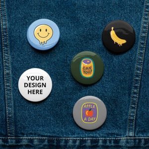 Könnte beinhalten: Fünf bunte Anstecknadeln mit verschiedenen Designs. Die Nadeln zeigen ein Smiley, eine Banane, eine Dose mit dem Text "Can You?", einen leeren weißen Kreis mit dem Text "Your Design Here" und einen Apfel mit dem Text "Apple A Day".