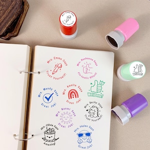K&ouml;nnte beinhalten: Eine Sammlung farbenfroher Stempel mit verschiedenen Designs und Phrasen wie "Vertraue dir selbst!", "Tolle Arbeit!" und "Gut gemacht!". Die Stempel sind in Rot, Pink, Gr&uuml;n und Lila gehalten und hinterlassen wei&szlig;e Abdr&uuml;cke auf wei&szlig;em Papier.