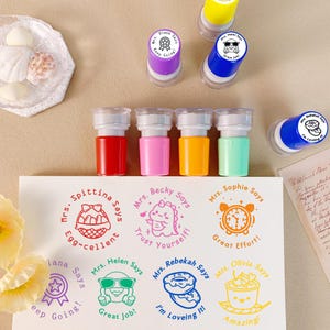 K&ouml;nnte beinhalten: Eine Sammlung farbenfroher Selbstf&auml;rbestempel mit verschiedenen Designs und Phrasen. Die Stempel enthalten S&auml;tze wie &bdquo;Egg-cellent&ldquo;, &bdquo;Great Job!&ldquo; und &bdquo;Amazing!&ldquo;. Die Stempel sind in Rot, Pink, Orange, Gr&uuml;n, Gelb und Blau.