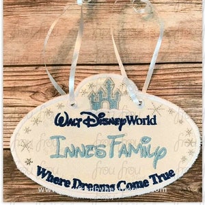 Op de afbeelding: Witte en blauwe geborduurde ornament met de tekst "Walt Disney World Innes Family Where Dreams Come True". De ornament heeft een blauw en wit geborduurd kasteel.